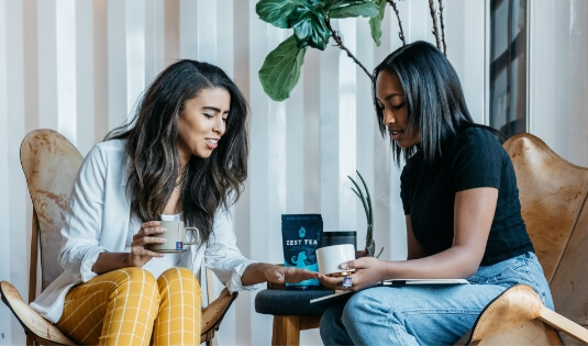  two diverse women, drinking coffee together.